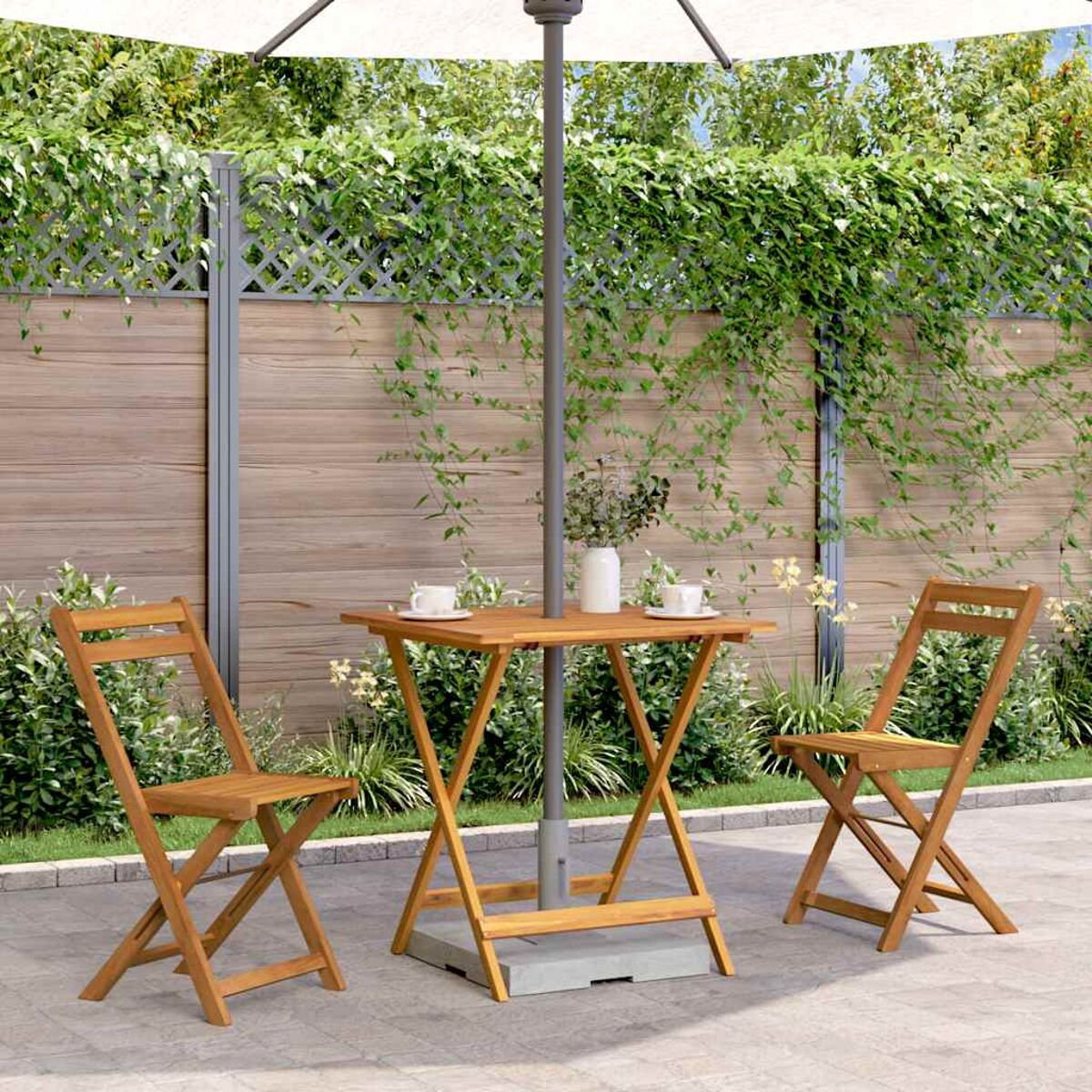 Holz-Terrassenset: Tisch, zwei Stühle und Sonnenschirm. Grünes Laub und Holzzaun im Hintergrund.