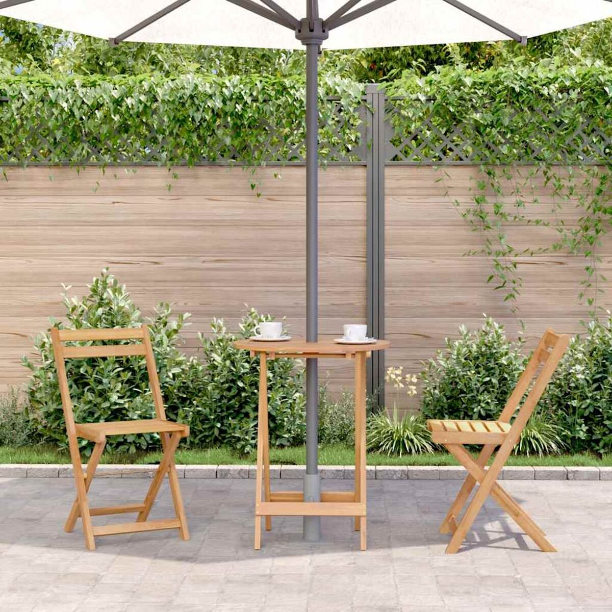 Eine Terrasse mit Tisch, zwei Stühlen und einem Sonnenschirm sowie Grün und einem Holzzaun.