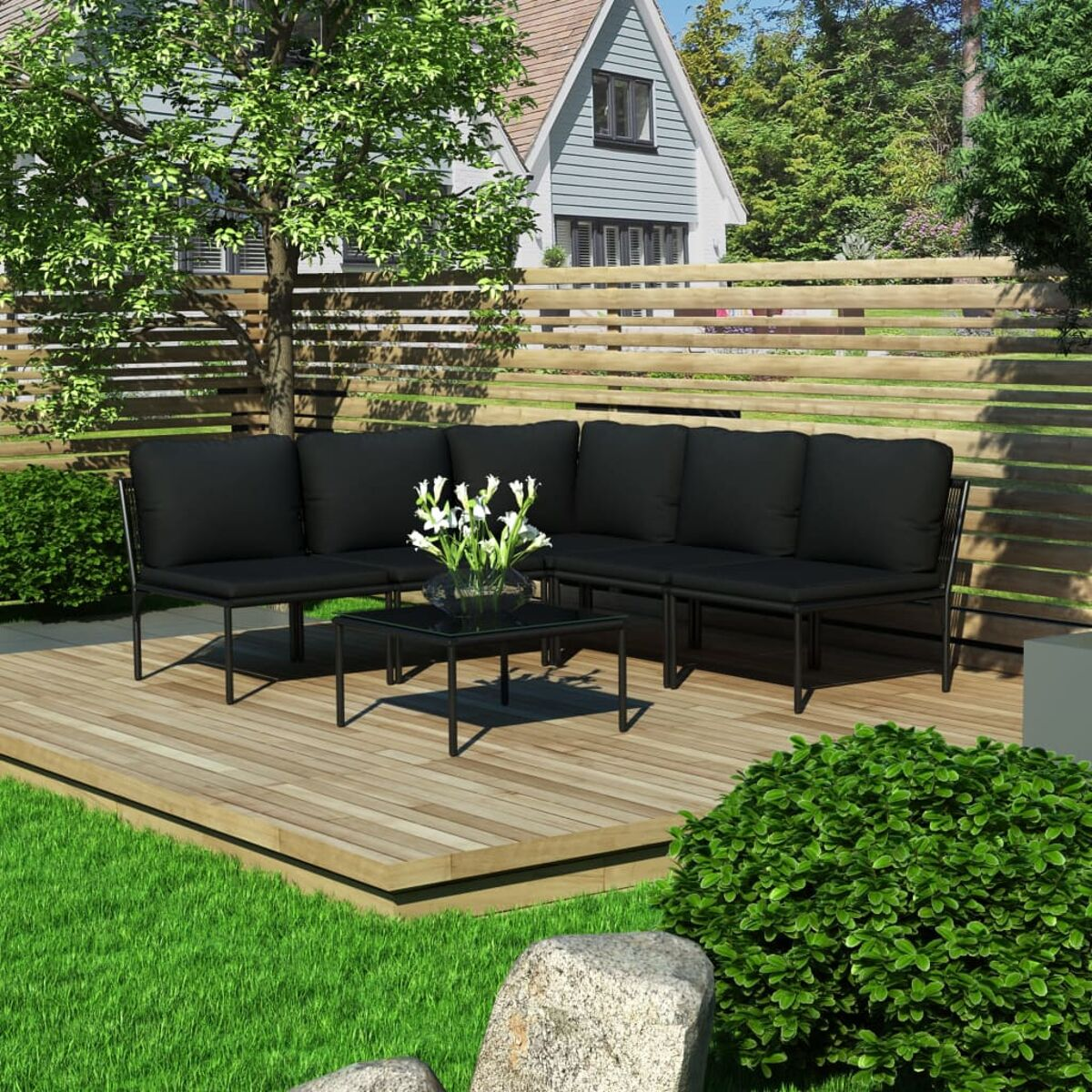 Gartenlounge-Set mit schwarzen Kissen, Glastisch, auf Holzterrasse. Grünes Gras und Haus im Hintergrund.