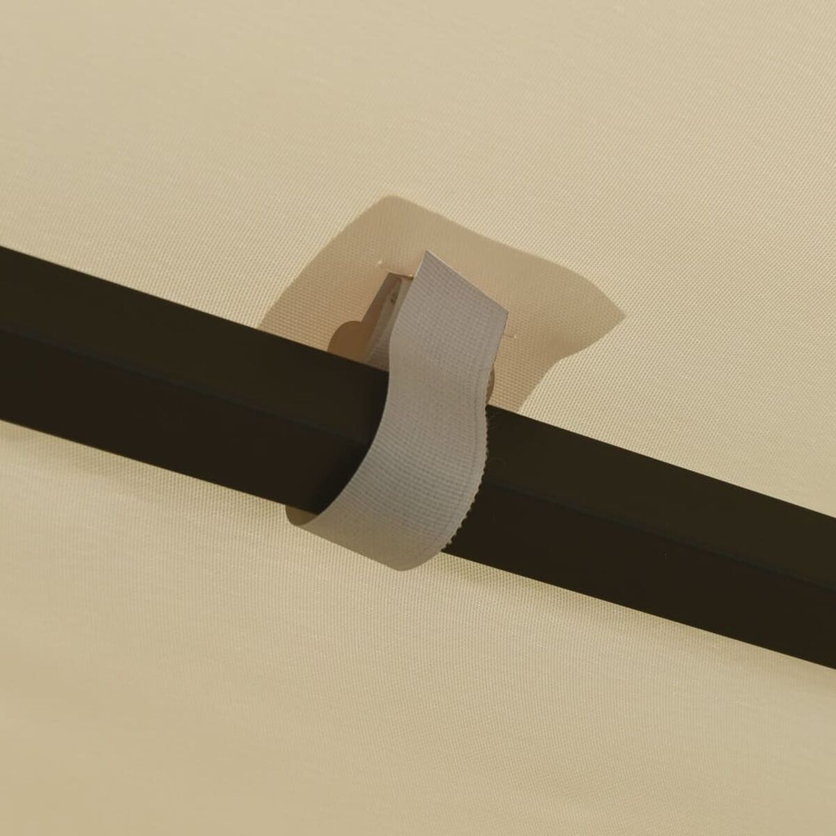 Nahaufnahme eines grauen Stoffriemens mit Klettverschluss, befestigt an einem schwarzen Metallstab, auf cremefarbenem Stoff.