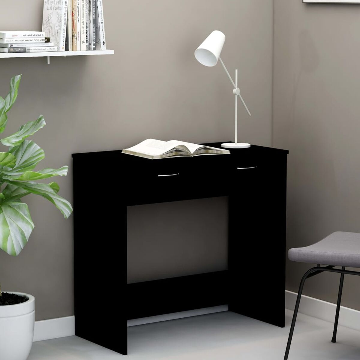 Schwarzer Schreibtisch mit Schubladen, Lampe und Buch. Neutrale Wand, Pflanze im Hintergrund.