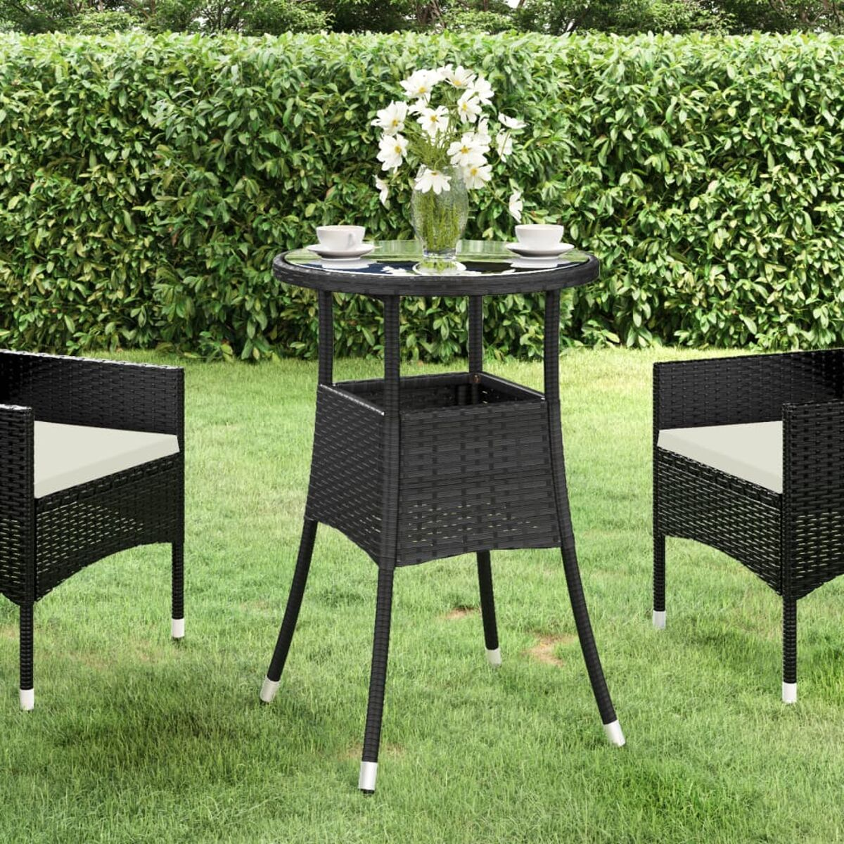 Szene im Freien mit einem schwarzen Korbtisch, zwei Stühlen und einem Blumenarrangement auf Rasen.