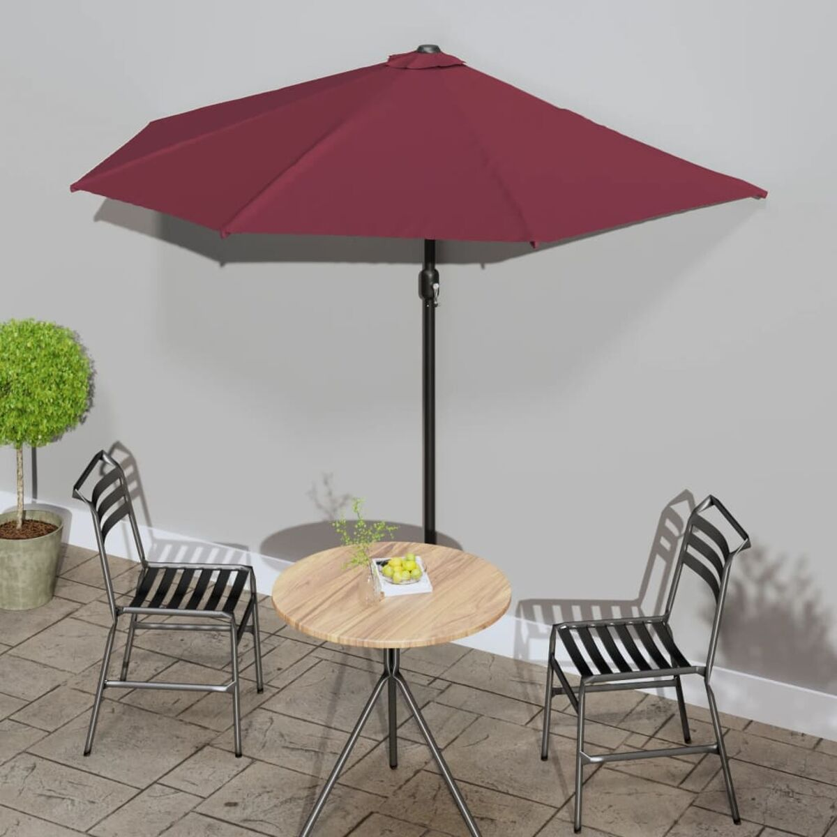 Runder Tisch mit rotem Schirm und zwei Stühlen auf einer Terrasse. Eine Pflanze.