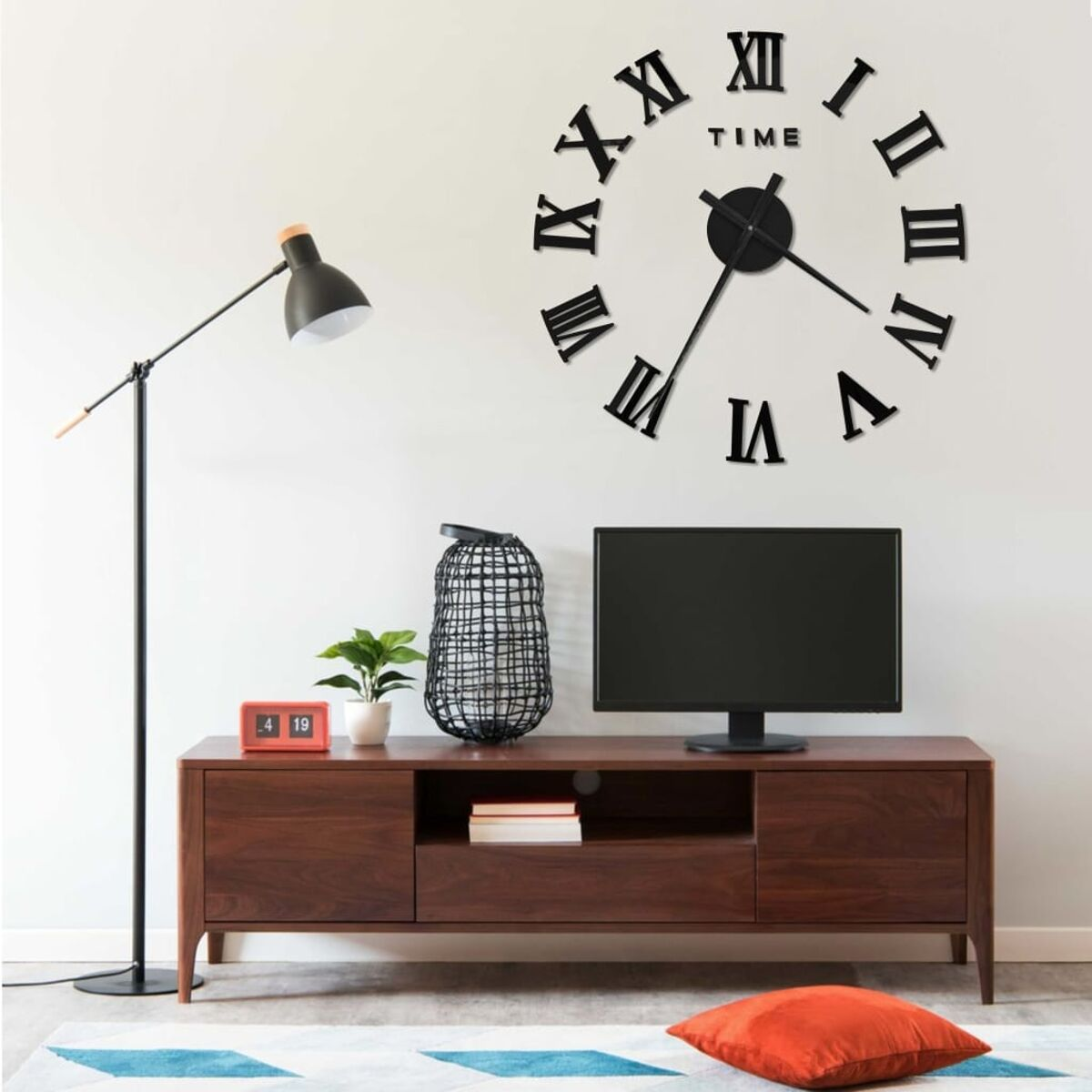 Wohnzimmer: Uhr, Fernseher und Schrank. Stehlampe und rotes Kissen ebenfalls sichtbar.