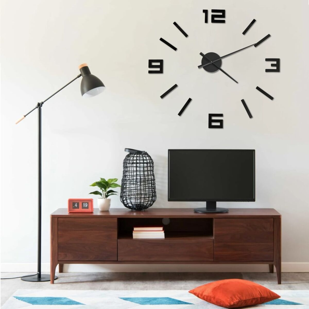 Eine Wanduhr mit schwarzen Ziffern und Zeigern. Ein Fernseher und Möbel sind unter der Uhr platziert.