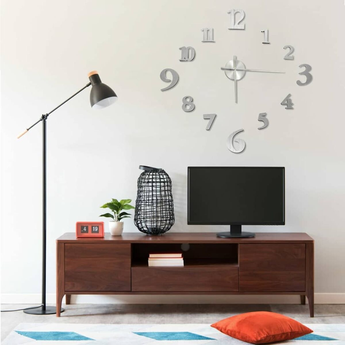 Wohnzimmer mit Uhr, Fernseher, Schrank, Stehlampe und rotem Kissen.