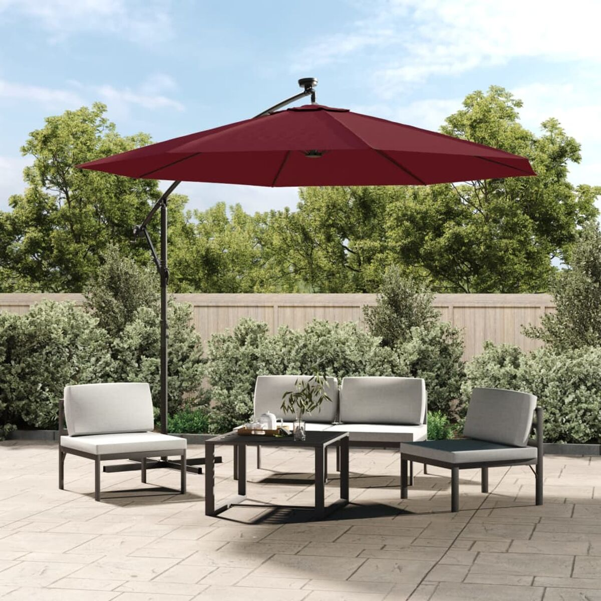 Terrassen-Set mit rotem Sonnenschirm, Sitzgruppe und kleinem Tisch, umgeben von Grün.