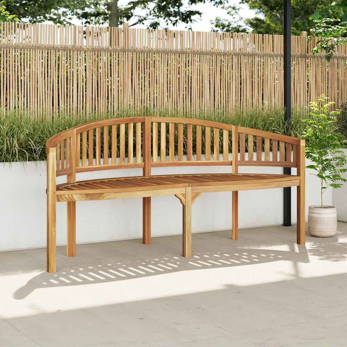 Eine Holzbank mit geschwungener Lehne auf einer Terrasse mit Bambuszäunen im Hintergrund.