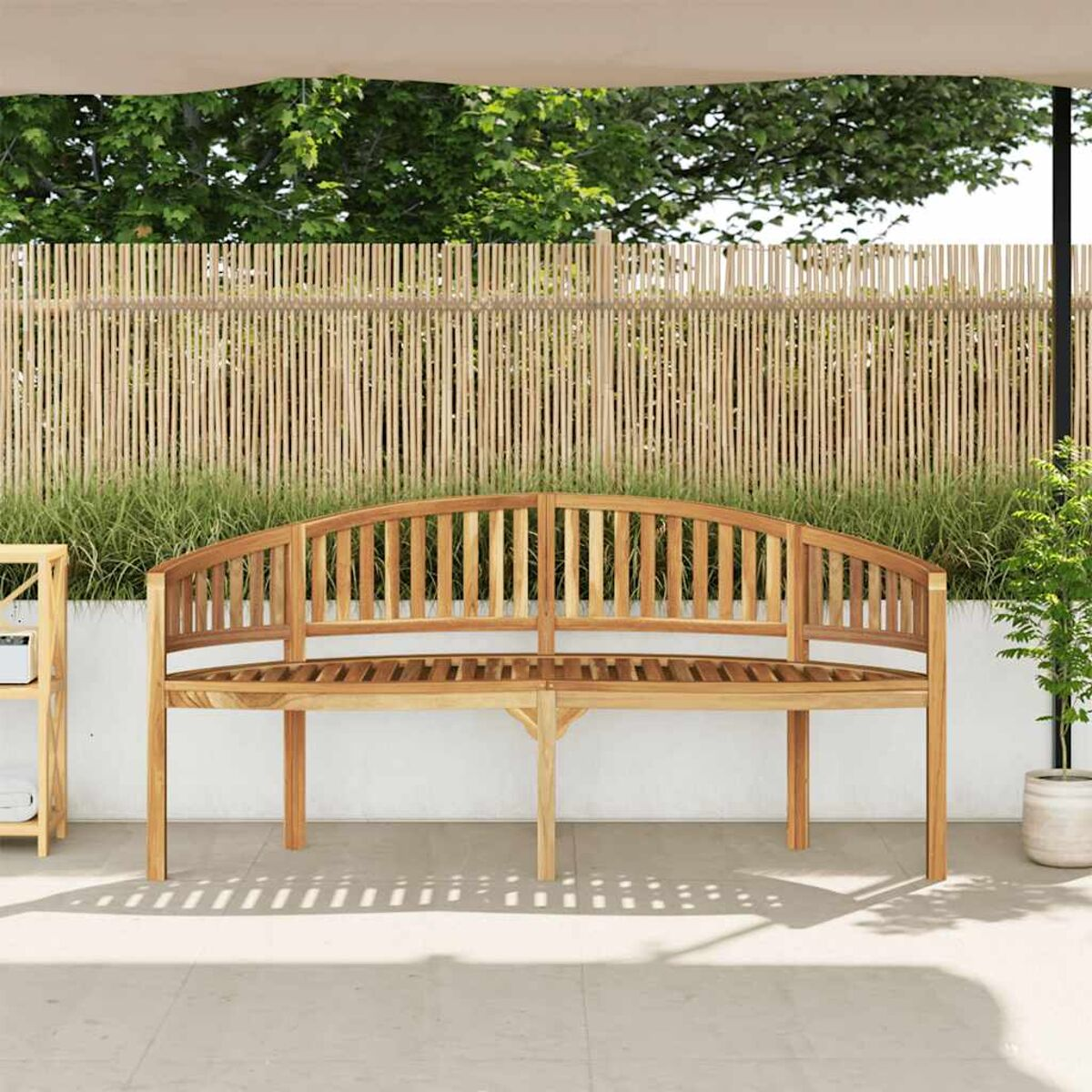 Eine Holzbank mit geschwungener Rückenlehne, auf einer Terrasse mit Pflanzen und Bambuszäunen dahinter.