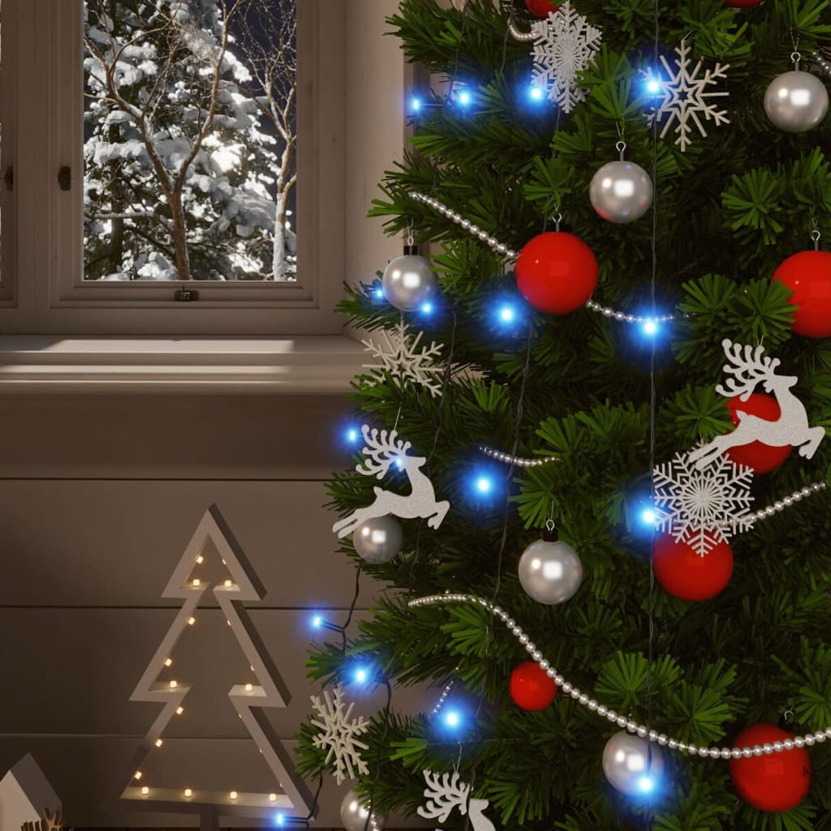 Weihnachtsbaum mit Ornamenten am Fenster. Schnee draußen.