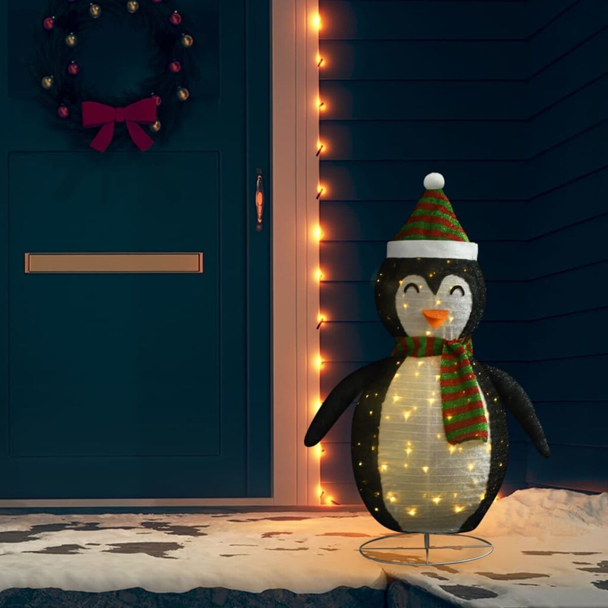 Beleuchtete Pinguin-Dekoration mit Hut und Schal, vor einer Tür stehend.