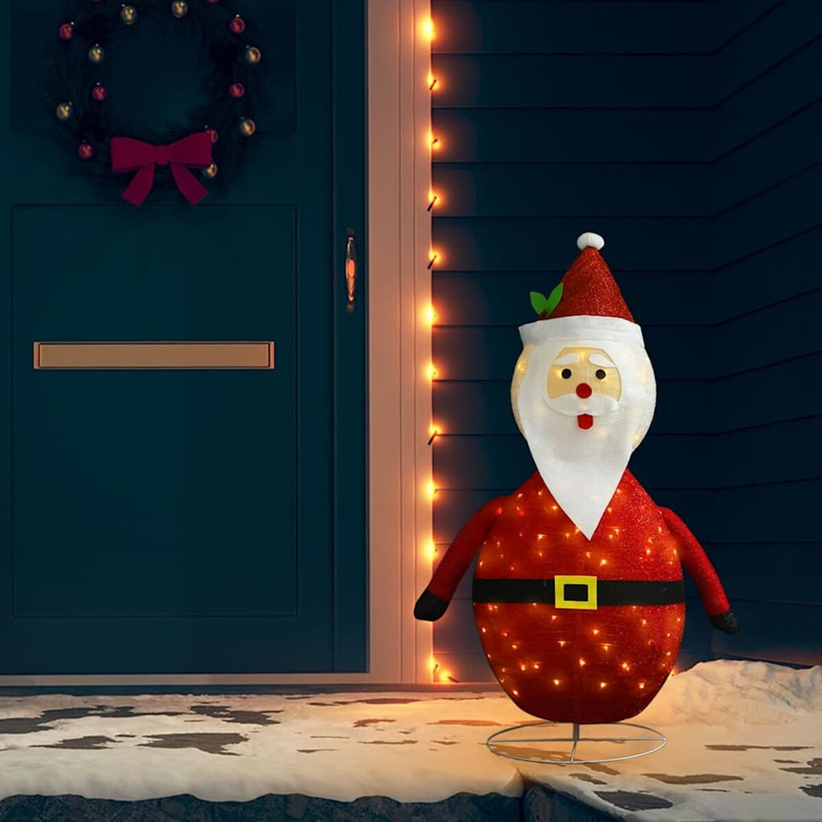 Weihnachtsmann-Dekoration mit Lichtern vor einer blauen Tür und Kranz.