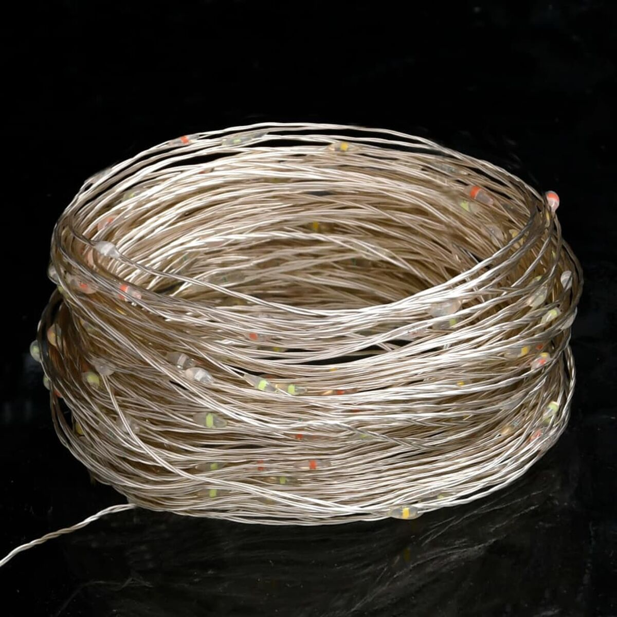 Aufgerollte Lichterkette mit kleinen, bunten Glühbirnen. Die Lichter liegen auf schwarzem Grund.