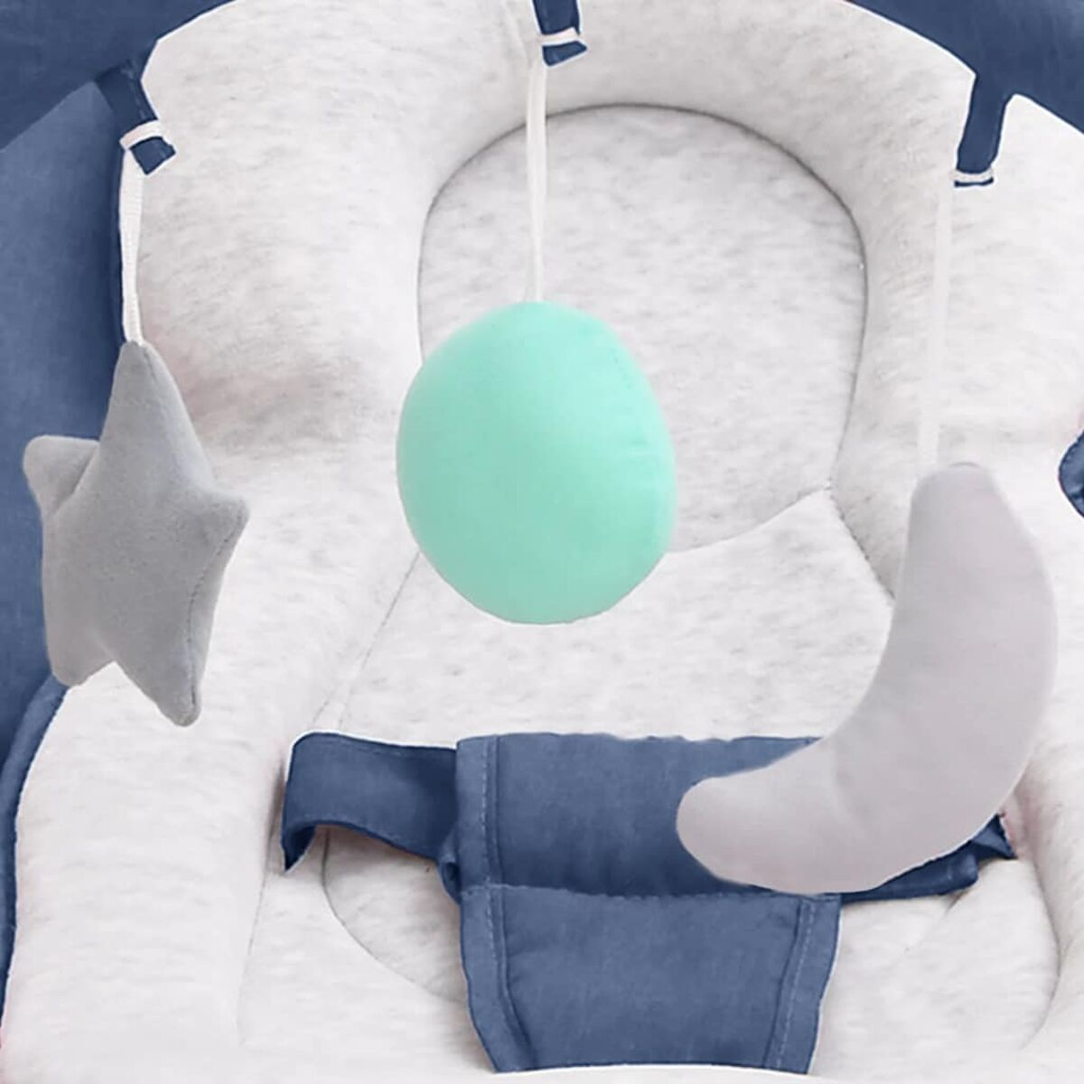 Nahaufnahme eines Baby-Wippers mit hängendem Spielzeug: Stern, Mond und ein grüner Ball.