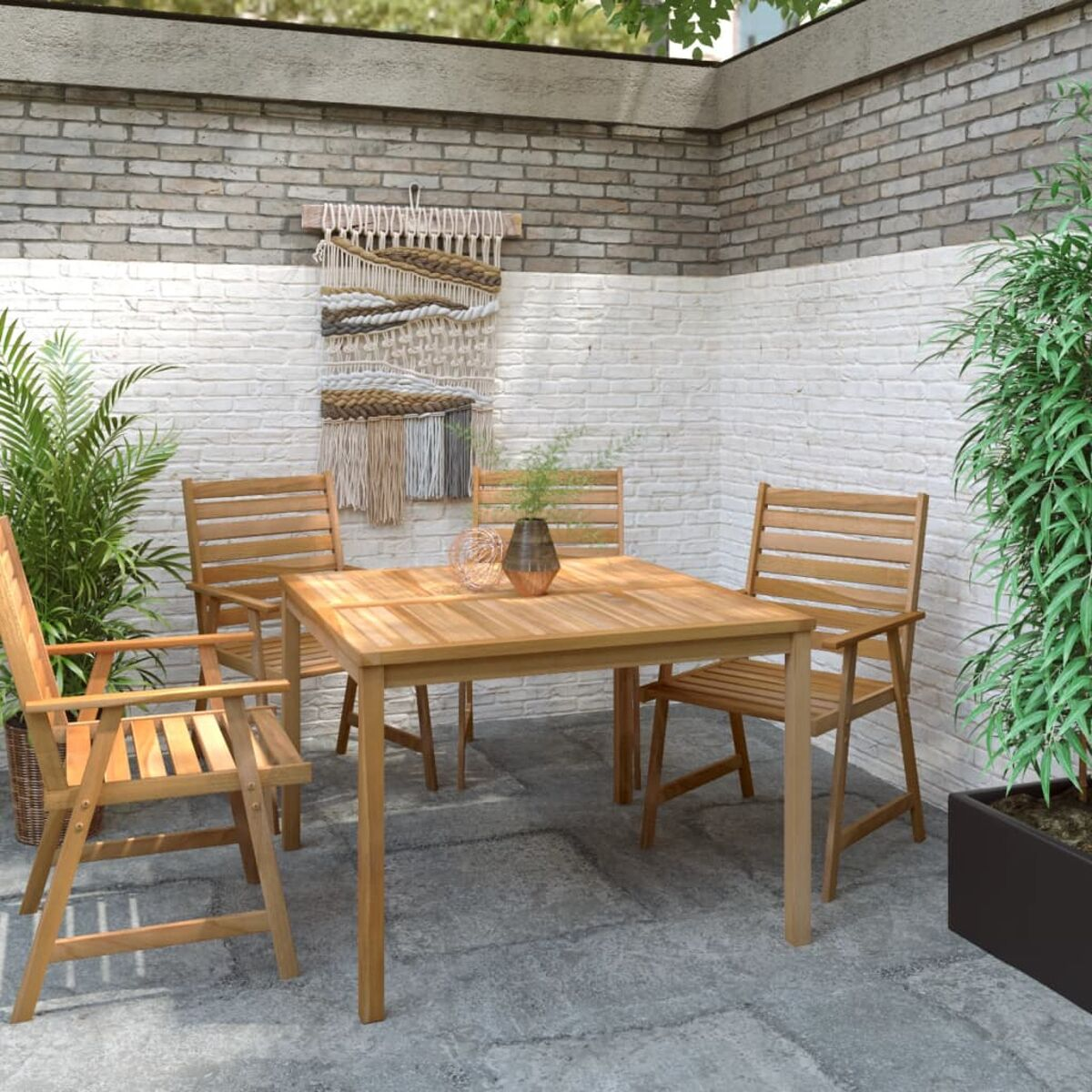Terrasse im Freien mit quadratischem Holztisch und Stühlen. Ein Wandteppich hängt an einer Ziegelmauer.