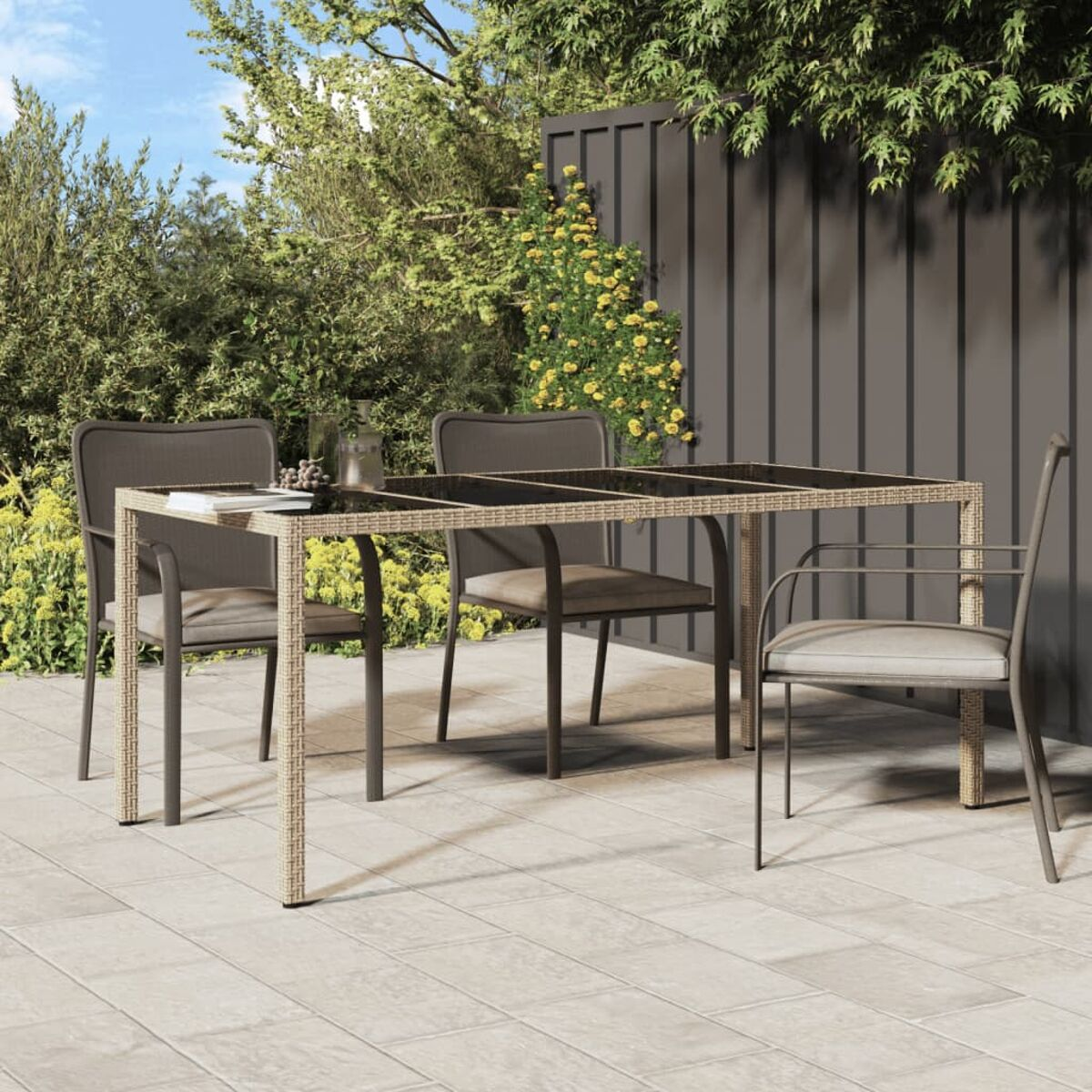 Terrasseneinrichtung mit Tisch und Stühlen. Hintergrund umfasst Garten und dunklen Zaun. Sonniger Tag.
