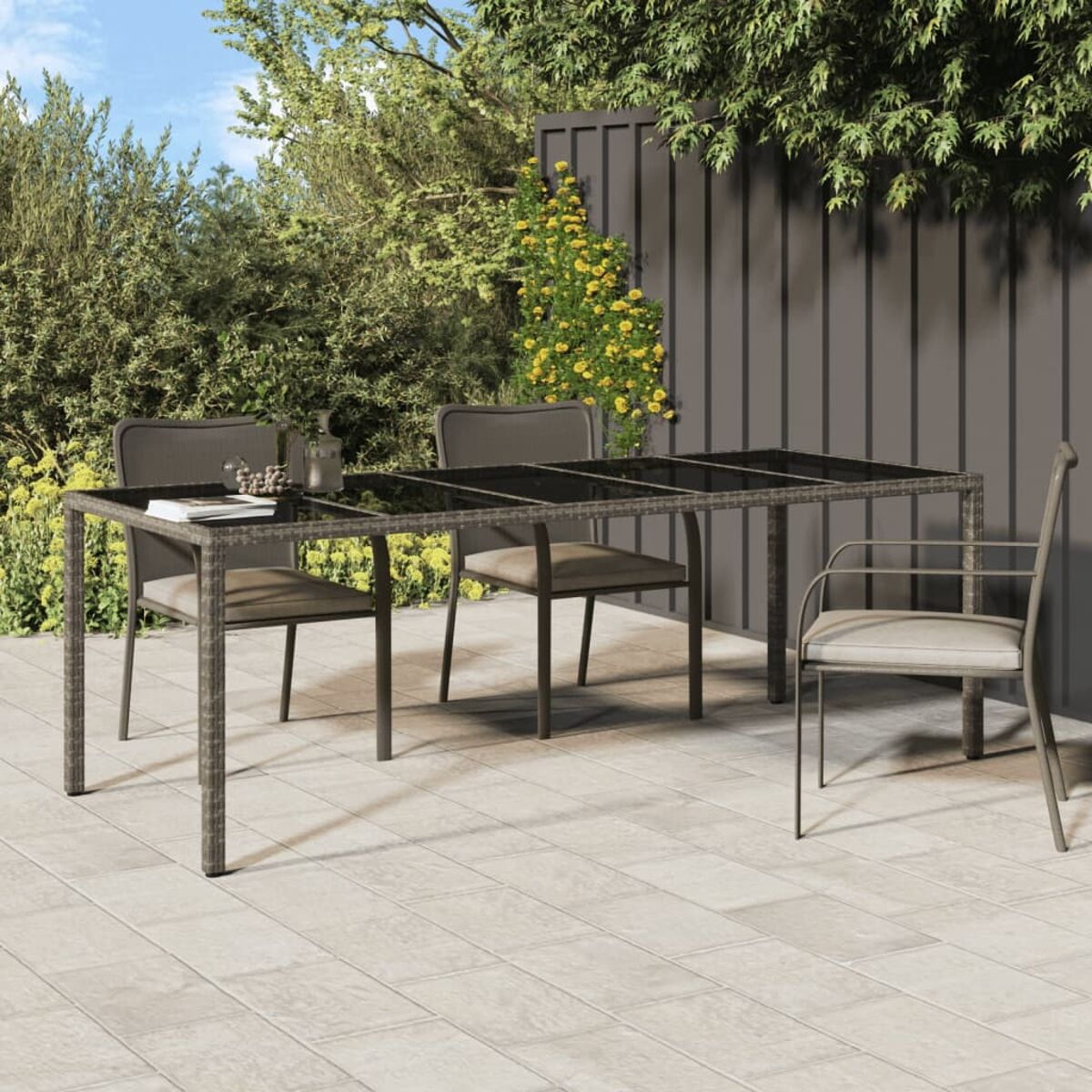 Rattantisch mit Glasplatte, vier Stühle. Outdoor-Setting mit Grün.