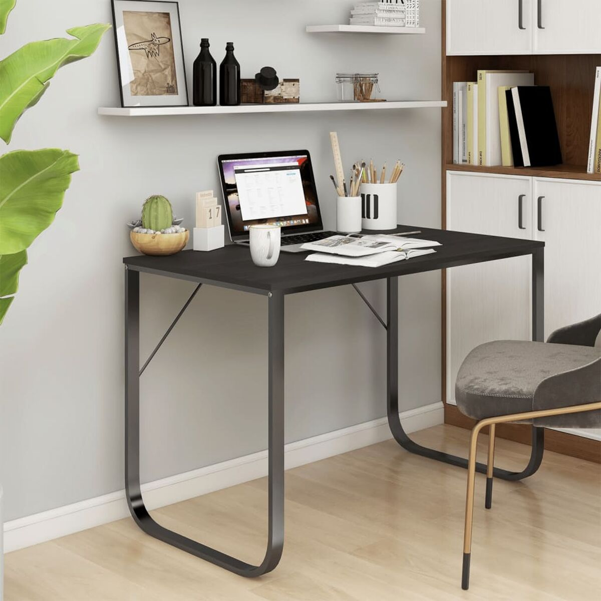 Schreibtisch mit Laptop, Becher, Kaktus, Stiften, Büchern und Kalender.