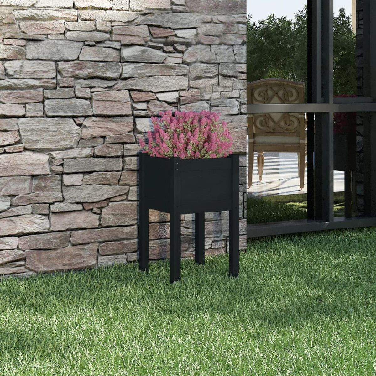 Ein schwarzer Pflanzkübel mit rosa Blumen auf grünem Gras, neben einer Backsteinmauer.