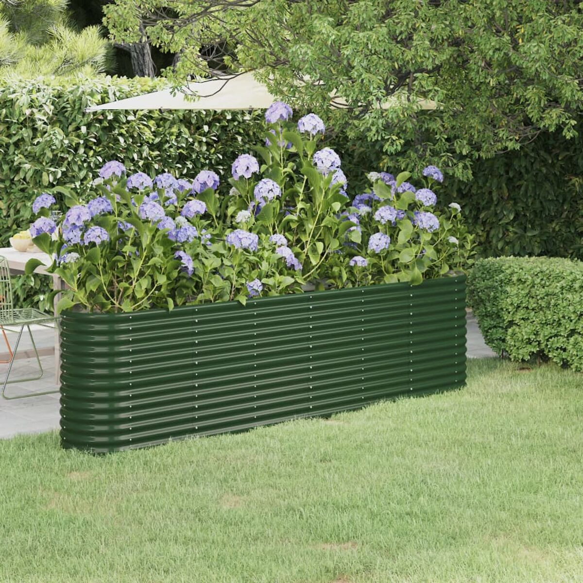 Ein grünes, wellblech Gartengrundbeet, gefüllt mit lila Blütenpflanzen und Gras.