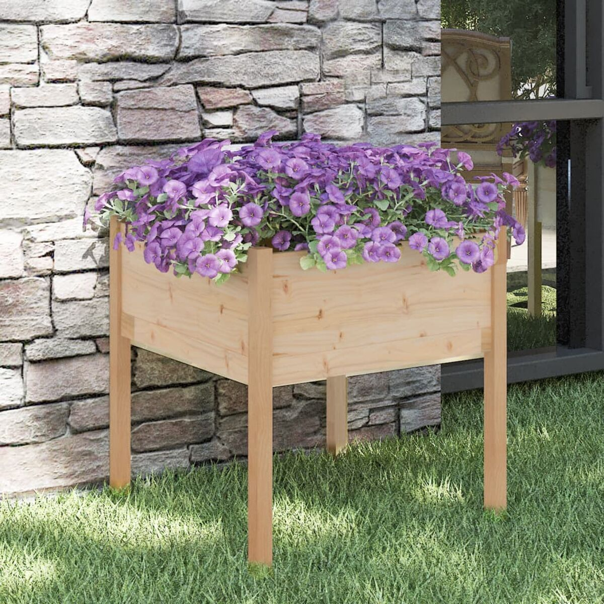 Erhöhtes Gartenbeet aus Holz mit lila Blumen. Vor einer Steinmauer und Gras.
