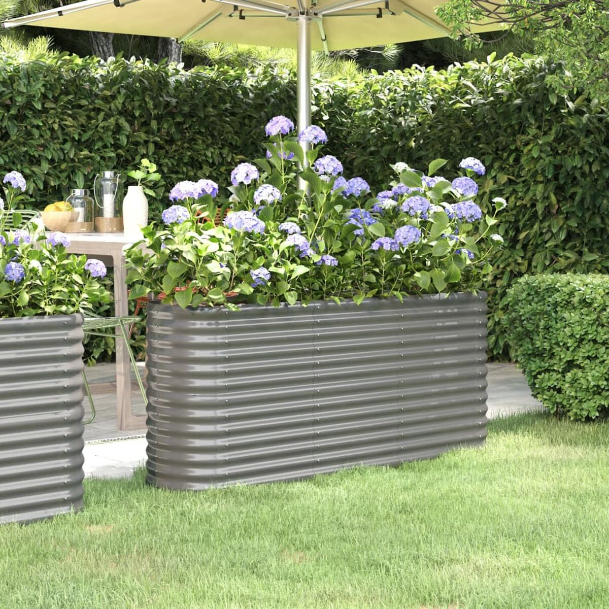 Gartenbeet mit gewelltem Metalldesign, gefüllt mit lila Blumen auf einem grünen Rasen, mit einem Tisch.