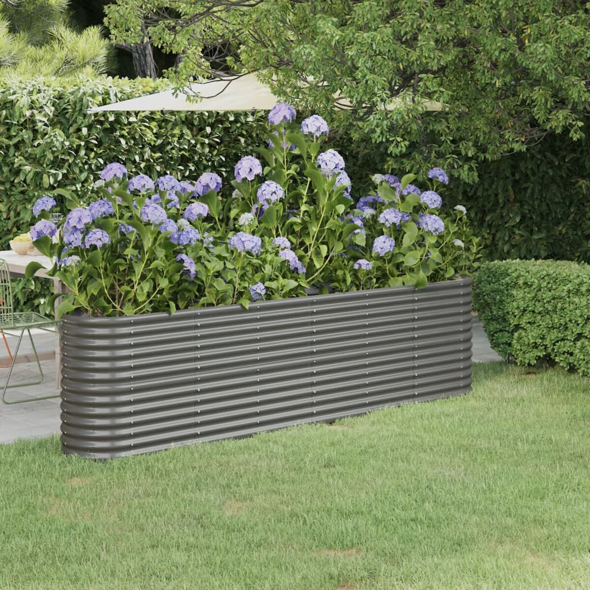 Metall-Gartenbeet mit dunkelgrauem Finish, gefüllt mit lila Hortensien auf einer Rasenfläche.