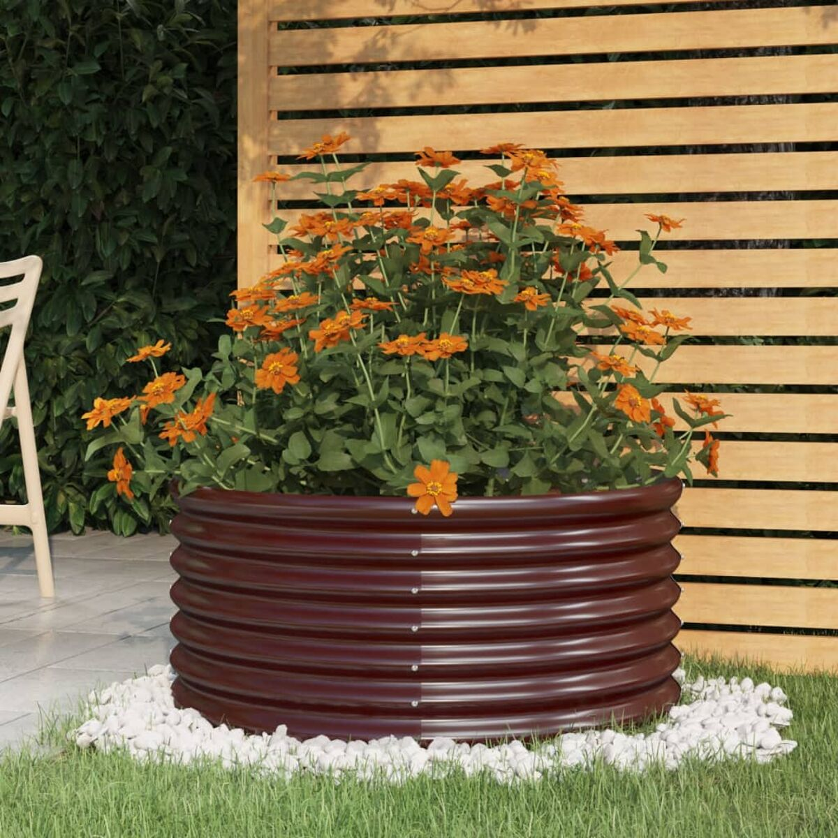 Runder, brauner Metallpflanzer mit orangefarbenen Blumen und weißen Steinen.