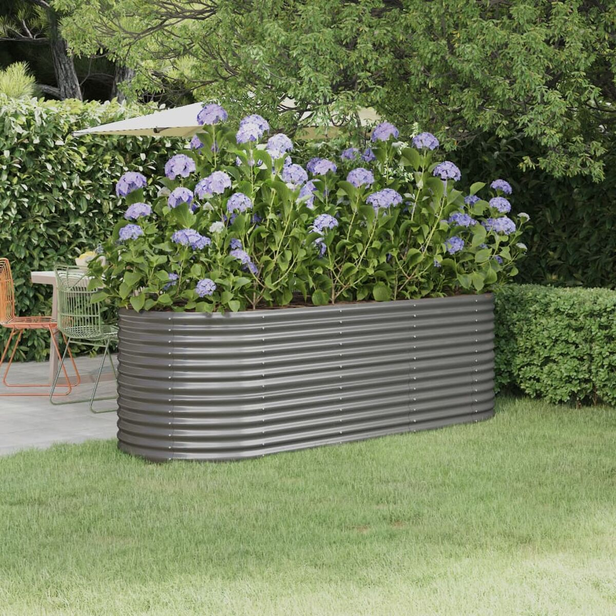 Erhöhtes Gartenbeet aus Metall mit lila Blumen. Grünes Gras und Hecken. Sonnige Umgebung im Freien.
