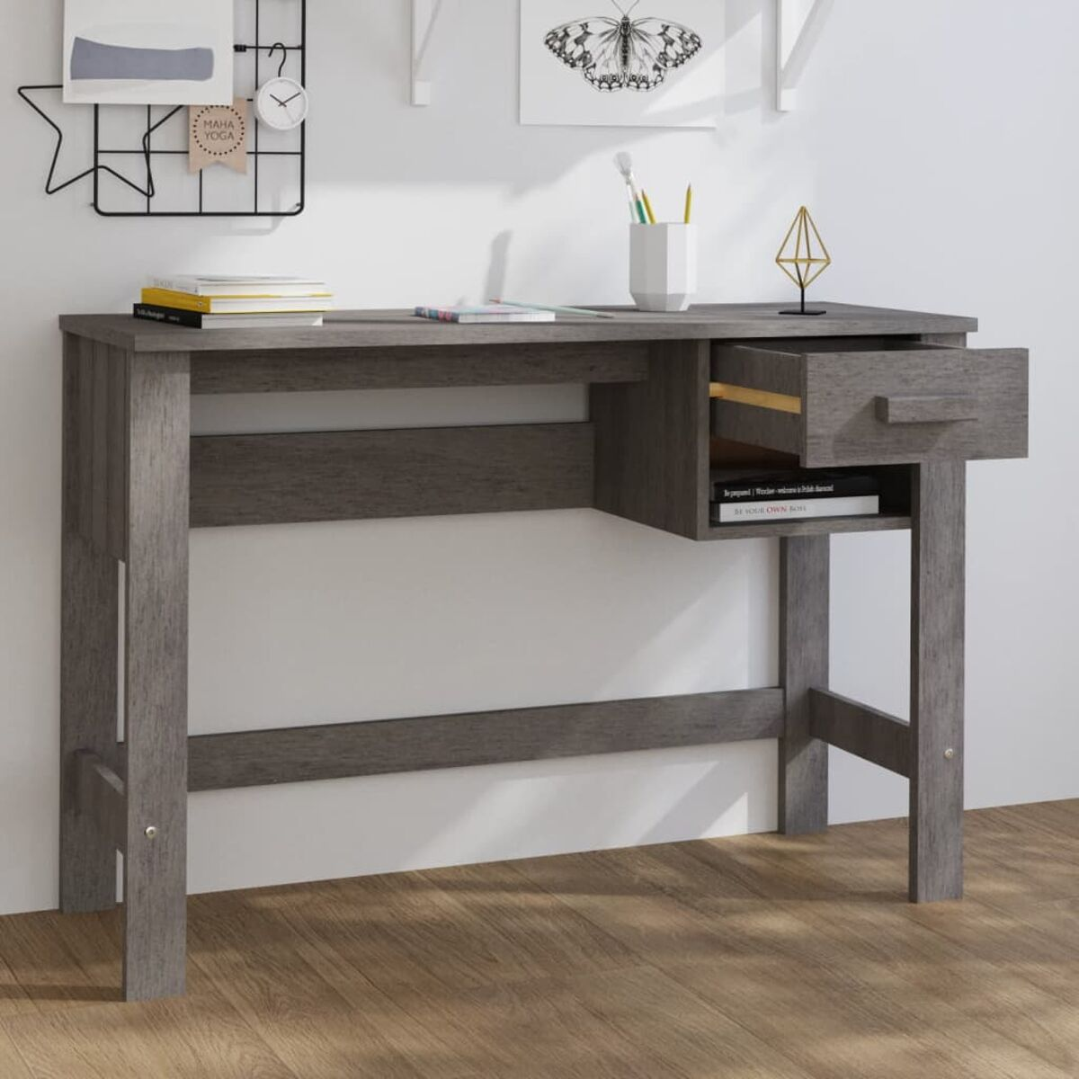 Grauer Holzschreibtisch mit offener Schublade. Bücher, Stifte und Dekoration oben. Weißer Wandhintergrund.