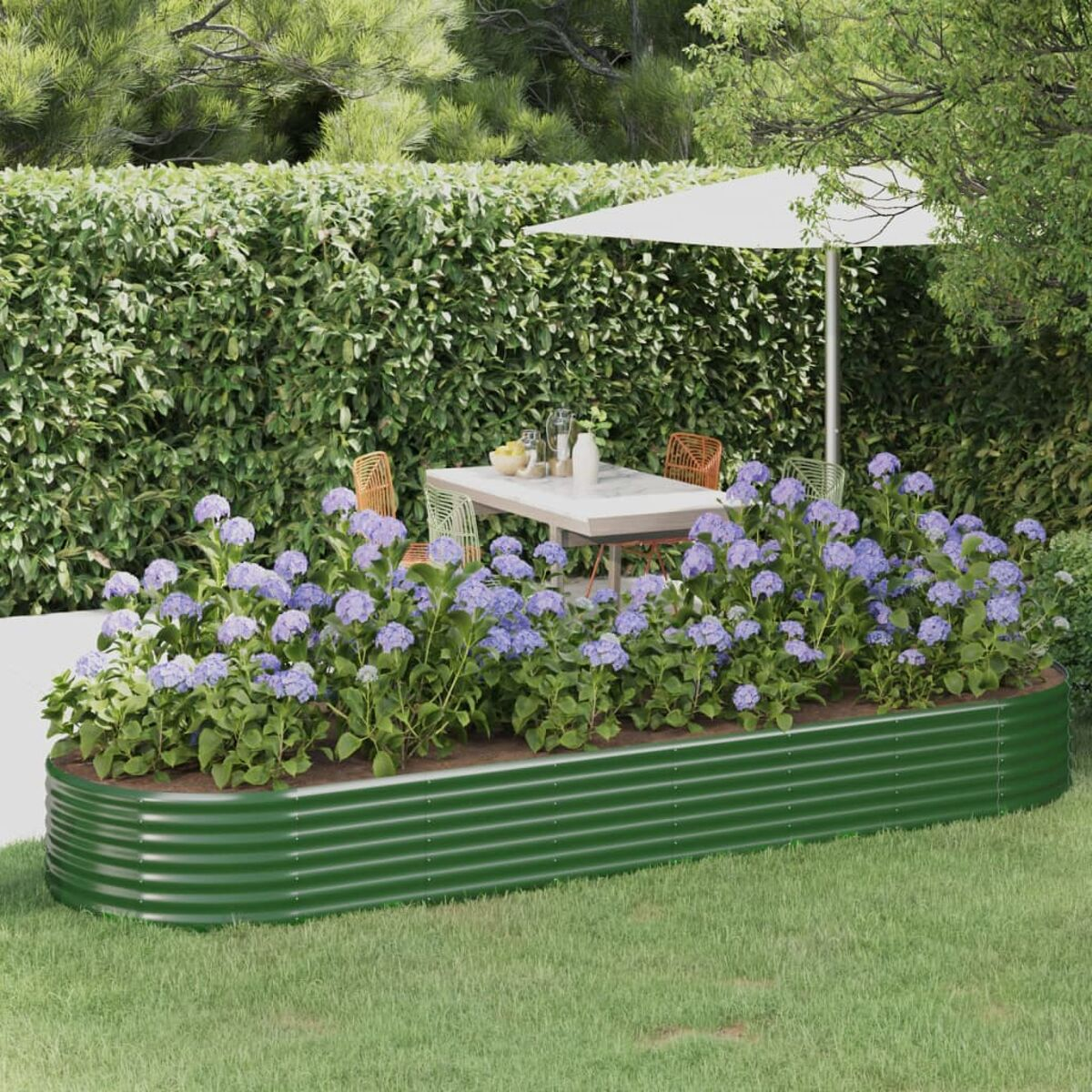 Grüner Metallpflanzkasten mit lila Blumen. Gartenszene mit Tisch und Sonnenschirm.