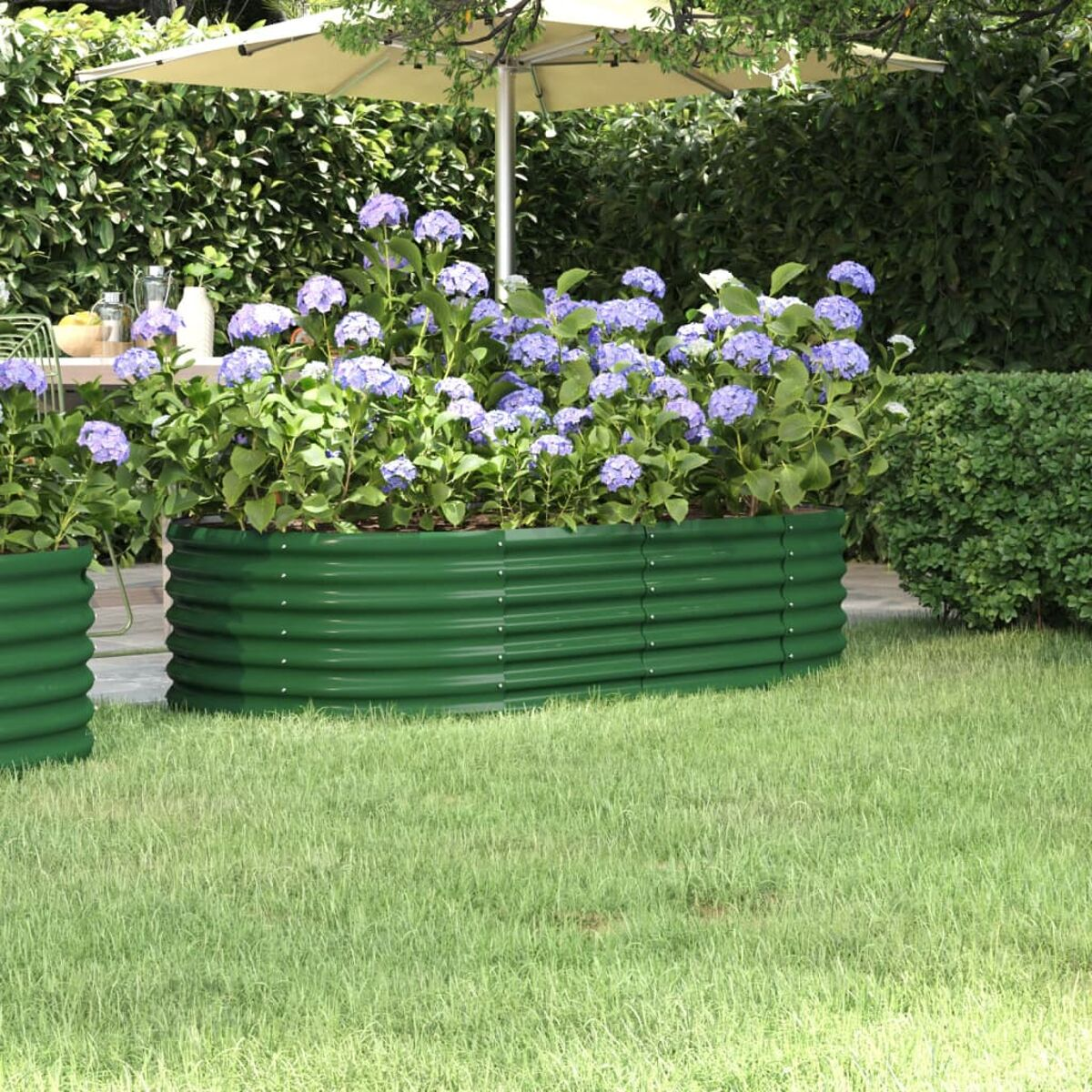Ein grüner Metallpflanzer gefüllt mit lila Blumen und grünem Laub, in einer Umgebung im Freien.