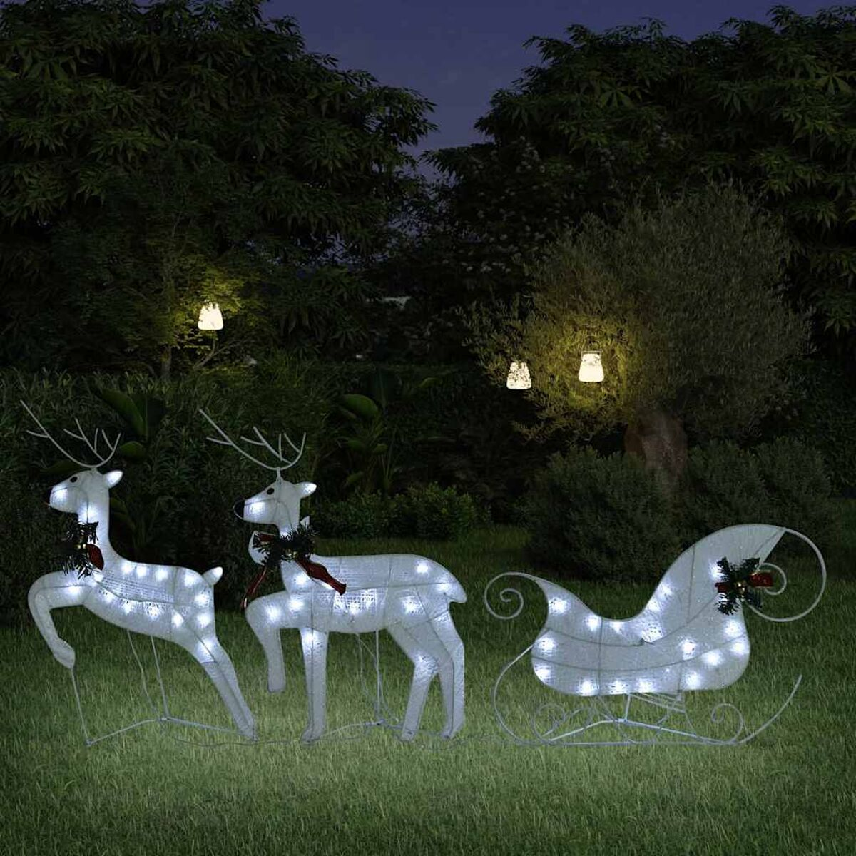 Weihnachtsdekorationen in einem Garten bei Nacht. Enthält Rentiere, einen Schlitten.