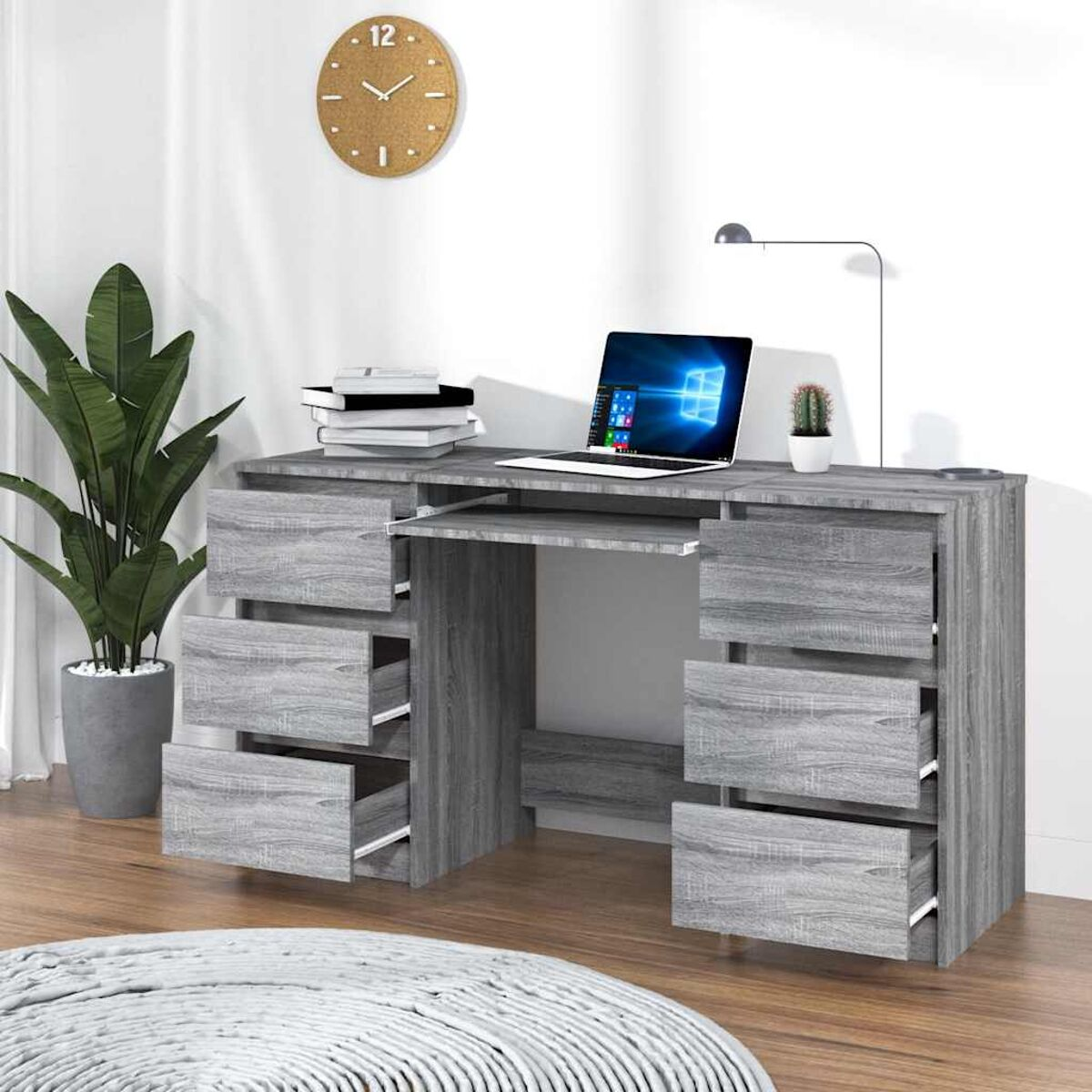 Grauer Schreibtisch mit Schubladen, Büchern und Laptop. Uhr und Pflanze an der Wand.