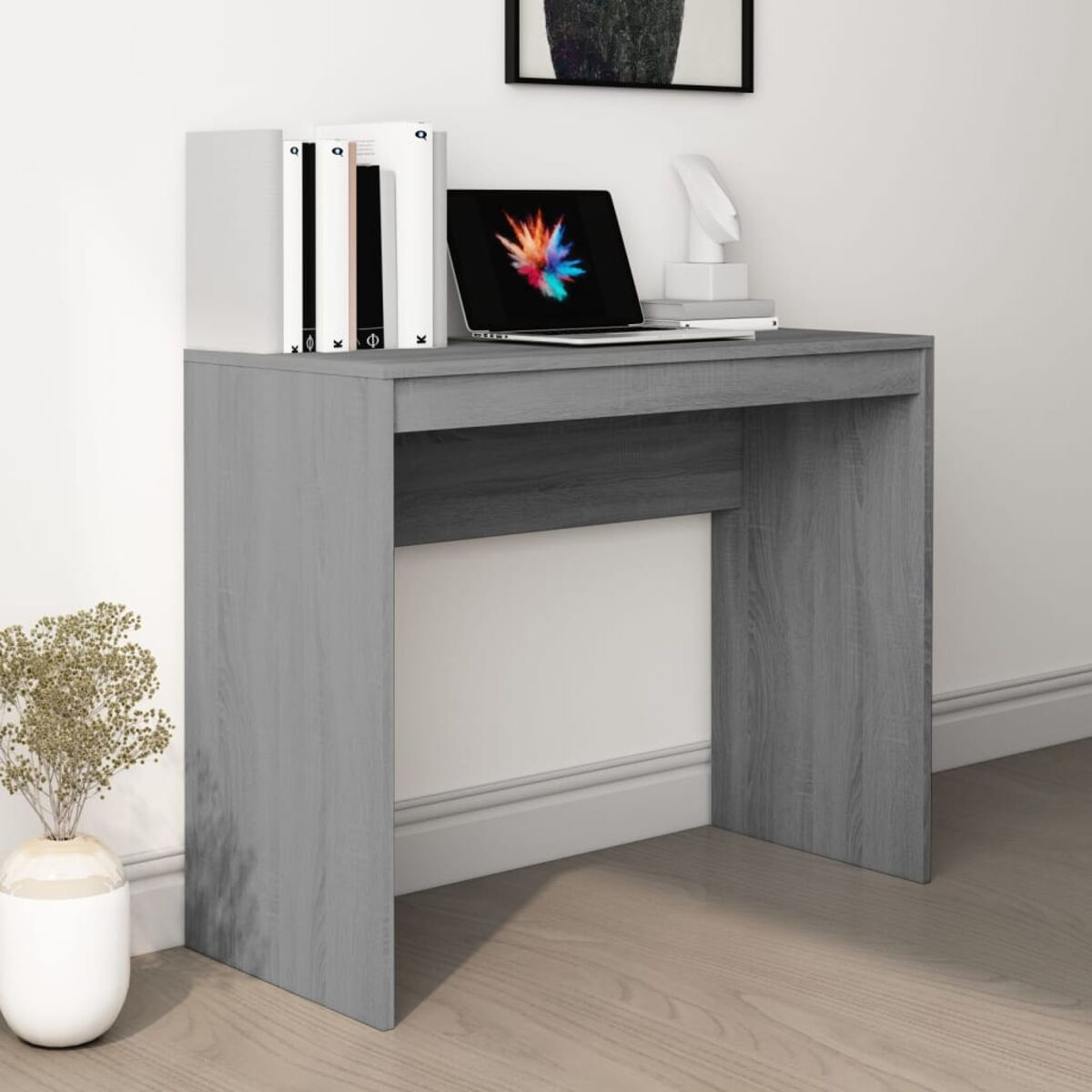 Ein grauer Holzschreibtisch mit Laptop und Büchern. Weißer Hintergrund und eine Vase mit trockenen Pflanzen.