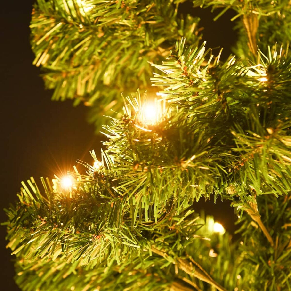 Nahaufnahme von Weihnachtsbaumzweigen mit funkelnden Lichtern, dunkler Hintergrund.