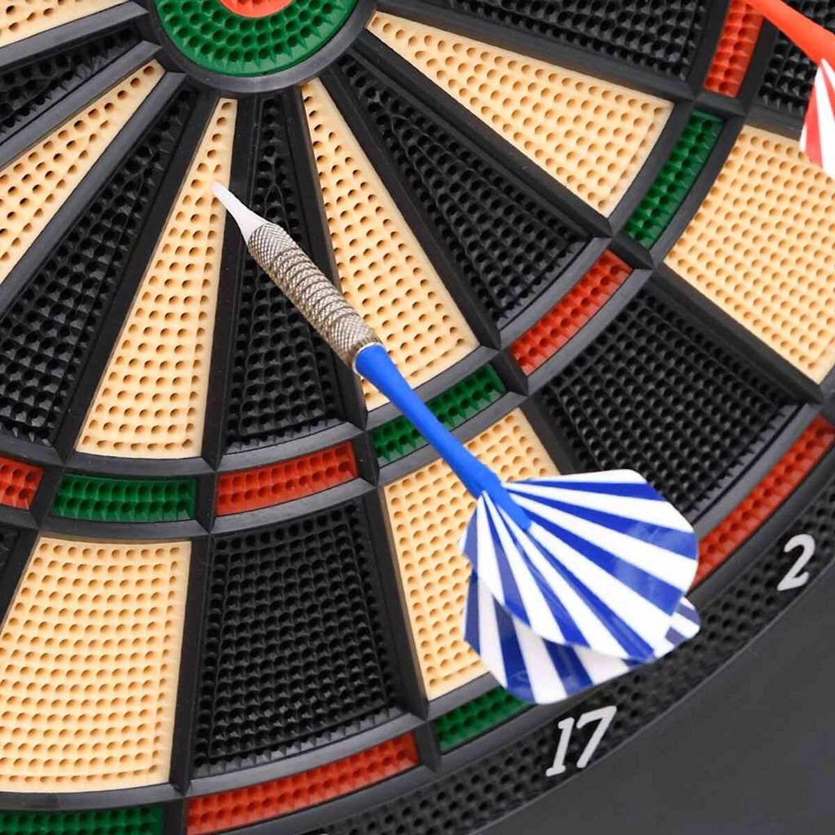 Ein Dart mit blau-weiß gestreiften Flights liegt auf einer schwarzen Dartscheibe mit grünen und gelben Abschnitten.