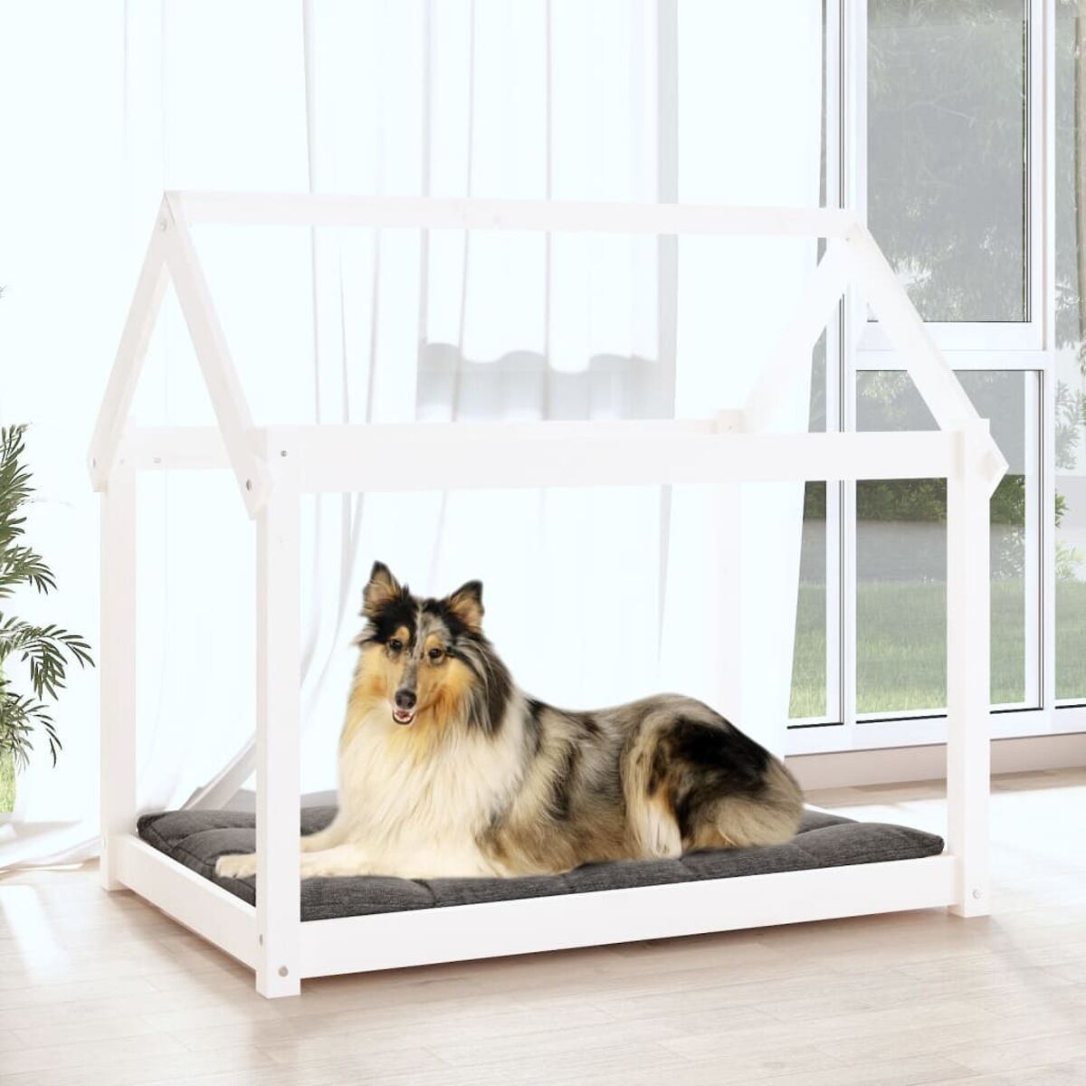 Ein Hund liegt auf einem grauen Bett in einem weißen hausförmigen Rahmen, in der Nähe eines Fensters.
