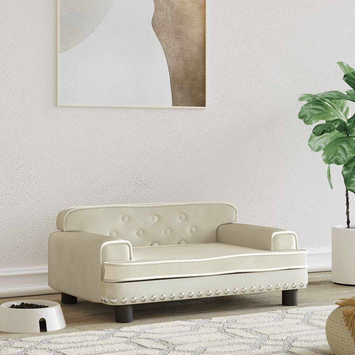 Cremefarbenes Hundesofa mit weißer Zierleiste und Knopfdetaills. Weiße Schüssel und Pflanze im Hintergrund.