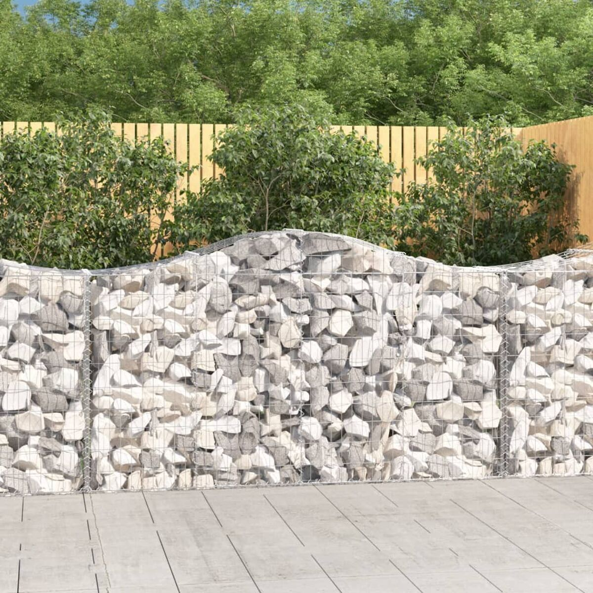 Eine Steinmauer mit gewellter Oberseite aus Felsen und einem Holzzaun mit grünem Hintergrund. Außenszene.