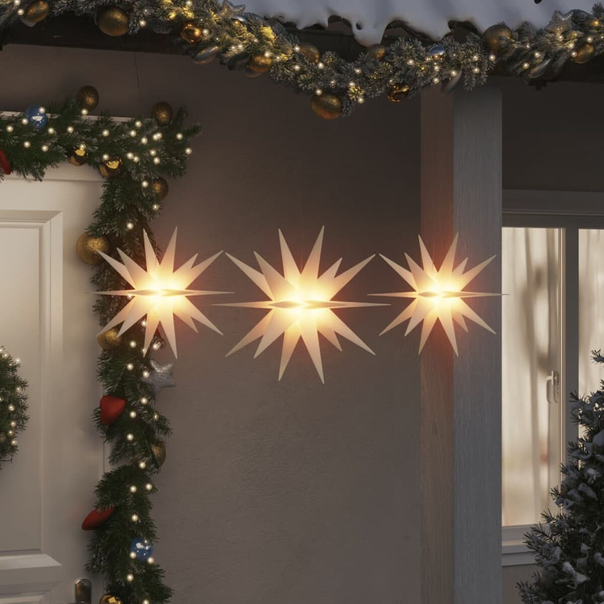 Drei sternförmige Weihnachtsbeleuchtungen hängen an einem Haus mit Dekorationen.