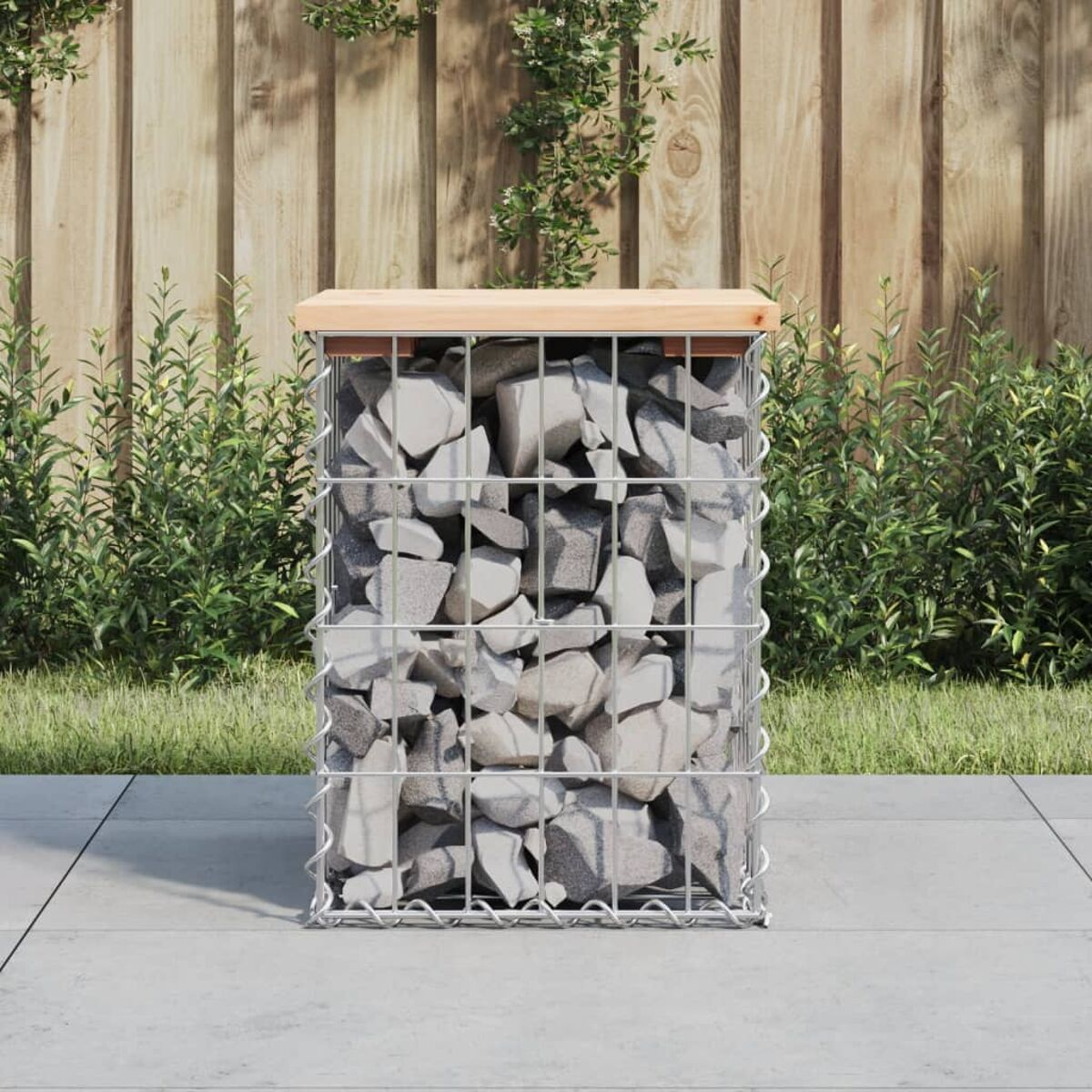 Ein Metallgabion mit Steinen im Inneren und einer Holzplatte, im Freien platziert.