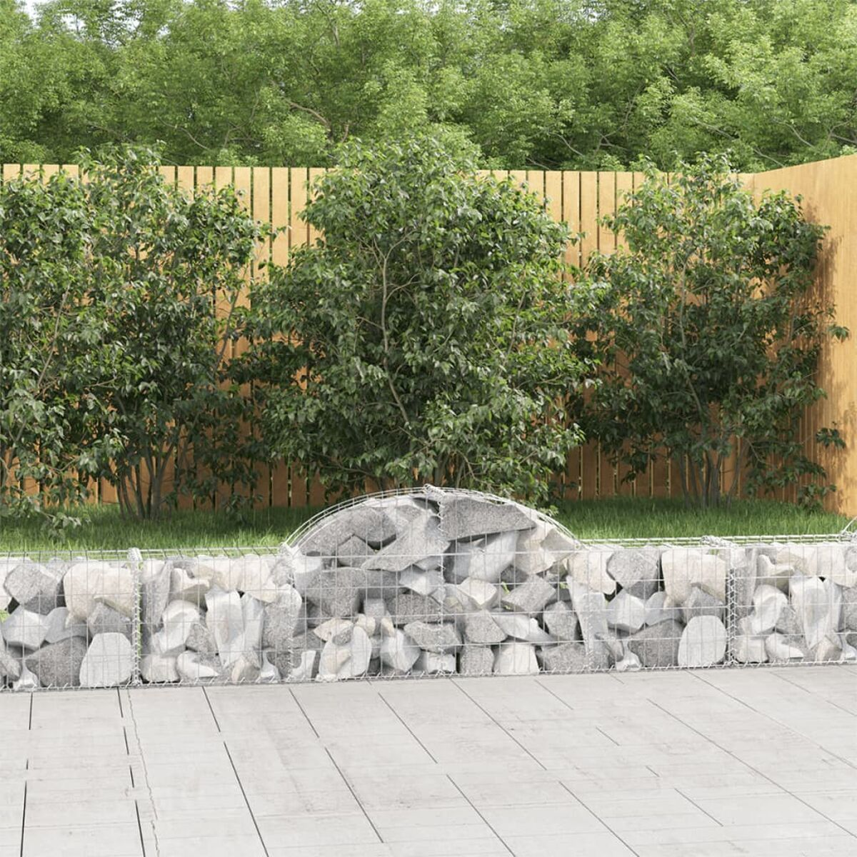 Eine Gartenszene mit einem Gabion und grünen Büschen. Ein Holzzaun im Hintergrund.