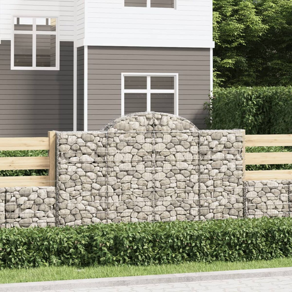 Ein Steinfence mit einem Haus im Hintergrund, einer grünen Hecke davor und einem gepflasterten Weg darunter.