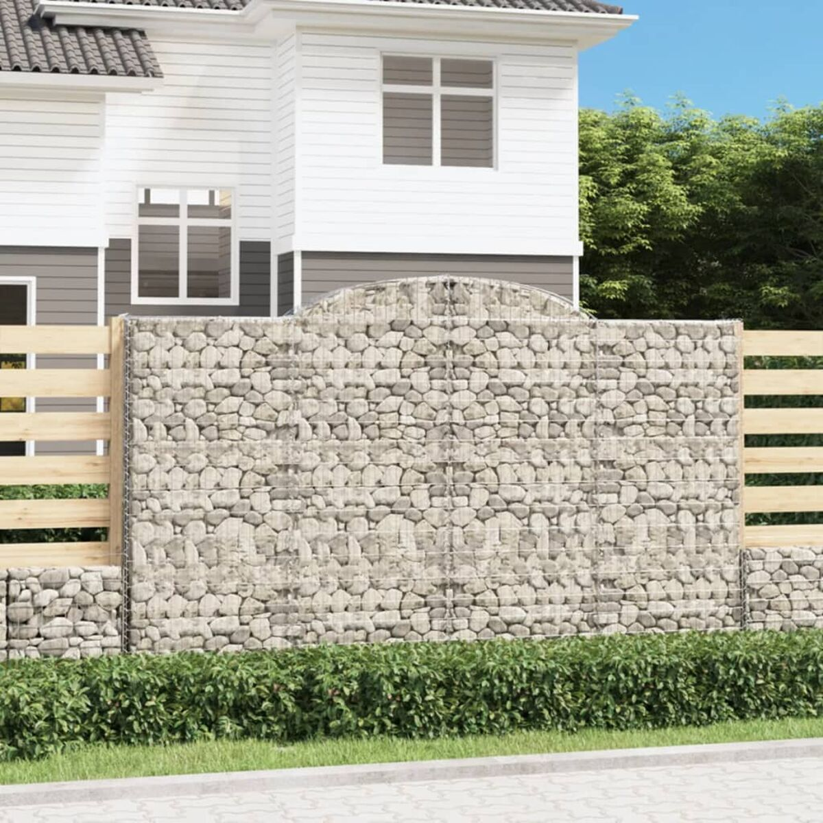 Ein Haus mit einer Steinmauer und einem Holzzaun. Bäume und Gras sind im Hintergrund.