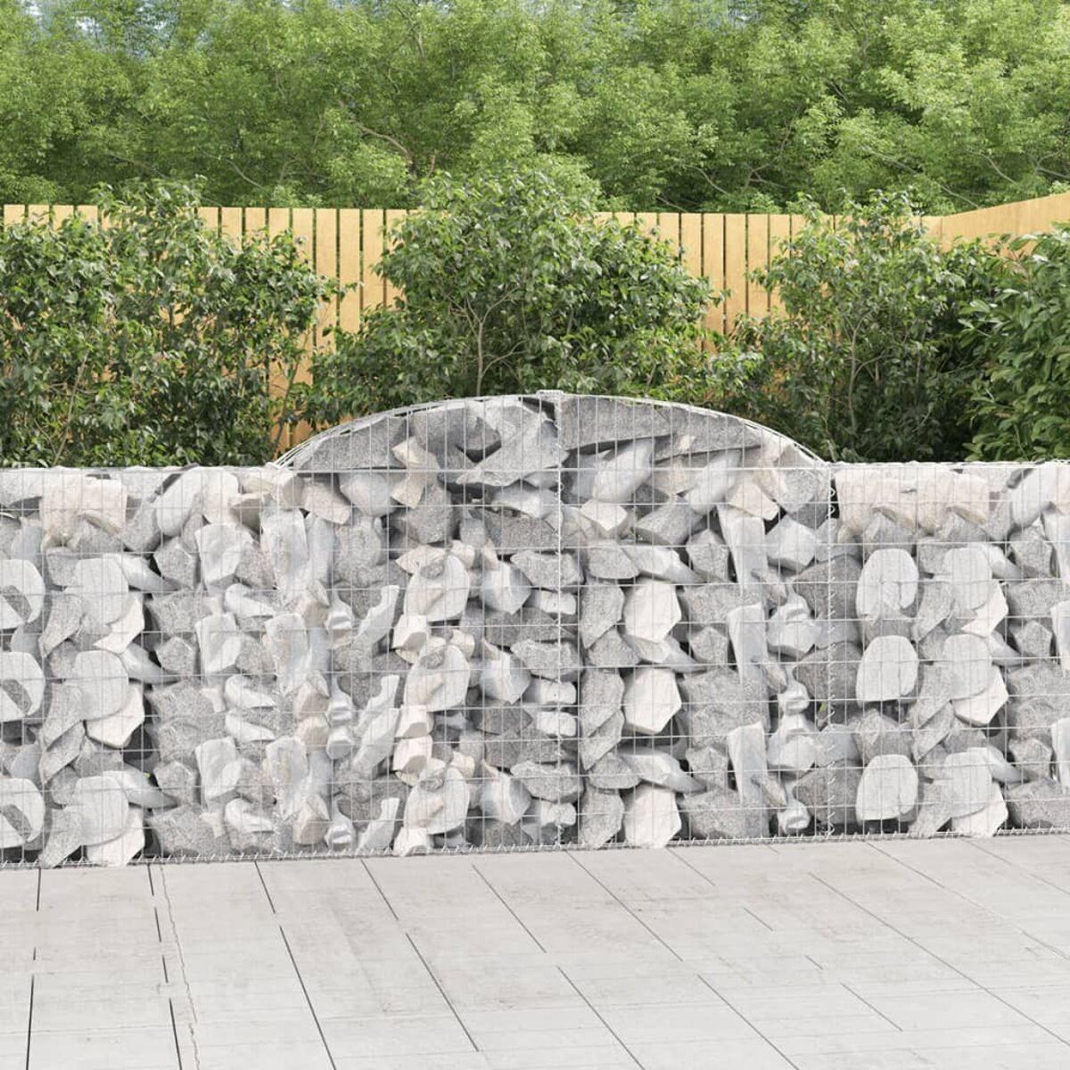 Steingabionenwand in einem Garten. Holzzaun und grüne Büsche im Hintergrund.