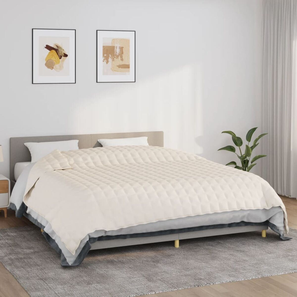 Bett mit cremefarbenem Steppbett und grauer Decke. Zwei gerahmte Bilder hängen über dem Bett.