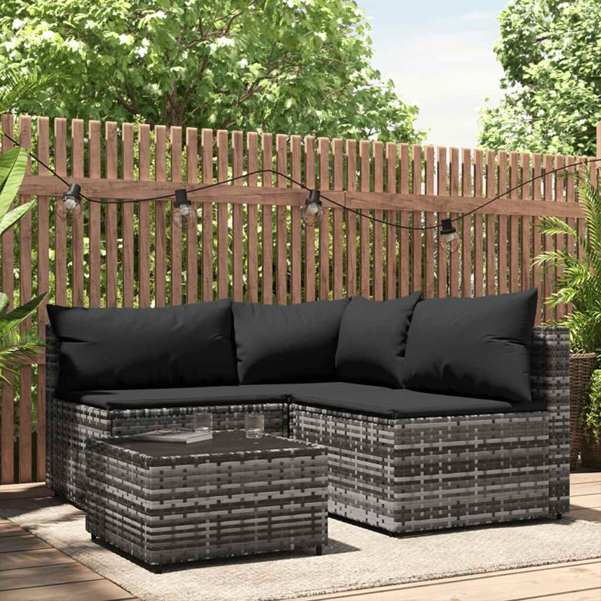 Outdoor-Rattansofa-Set mit schwarzen Kissen, vor Holzzaun.