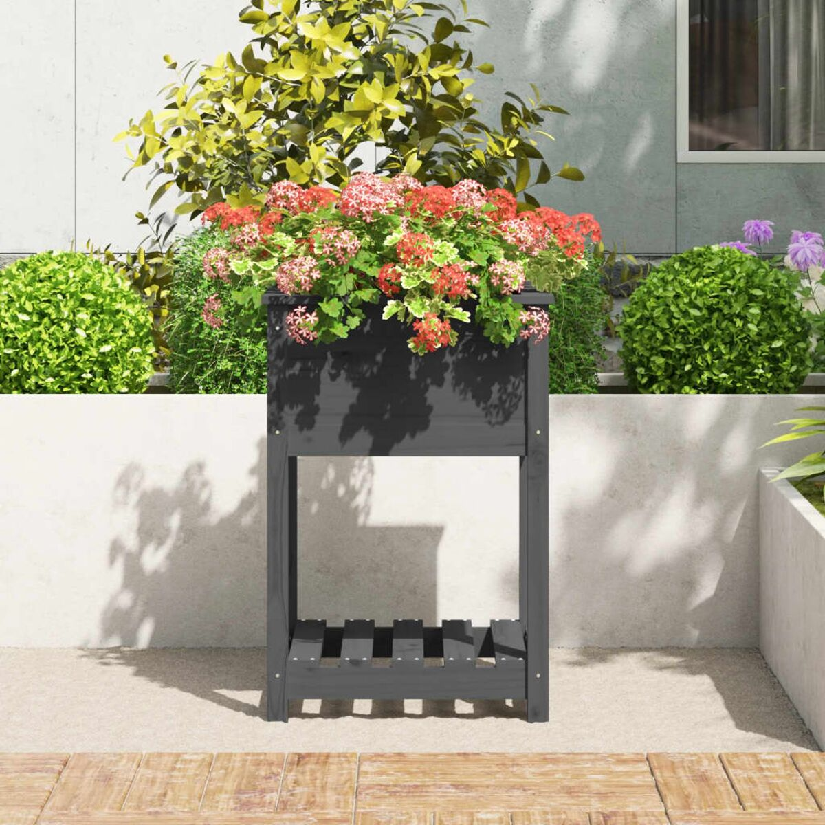 Dunkelgrauer Pflanzkasten mit Blumen. Der Hintergrund ist eine Wand und Pflanzen.