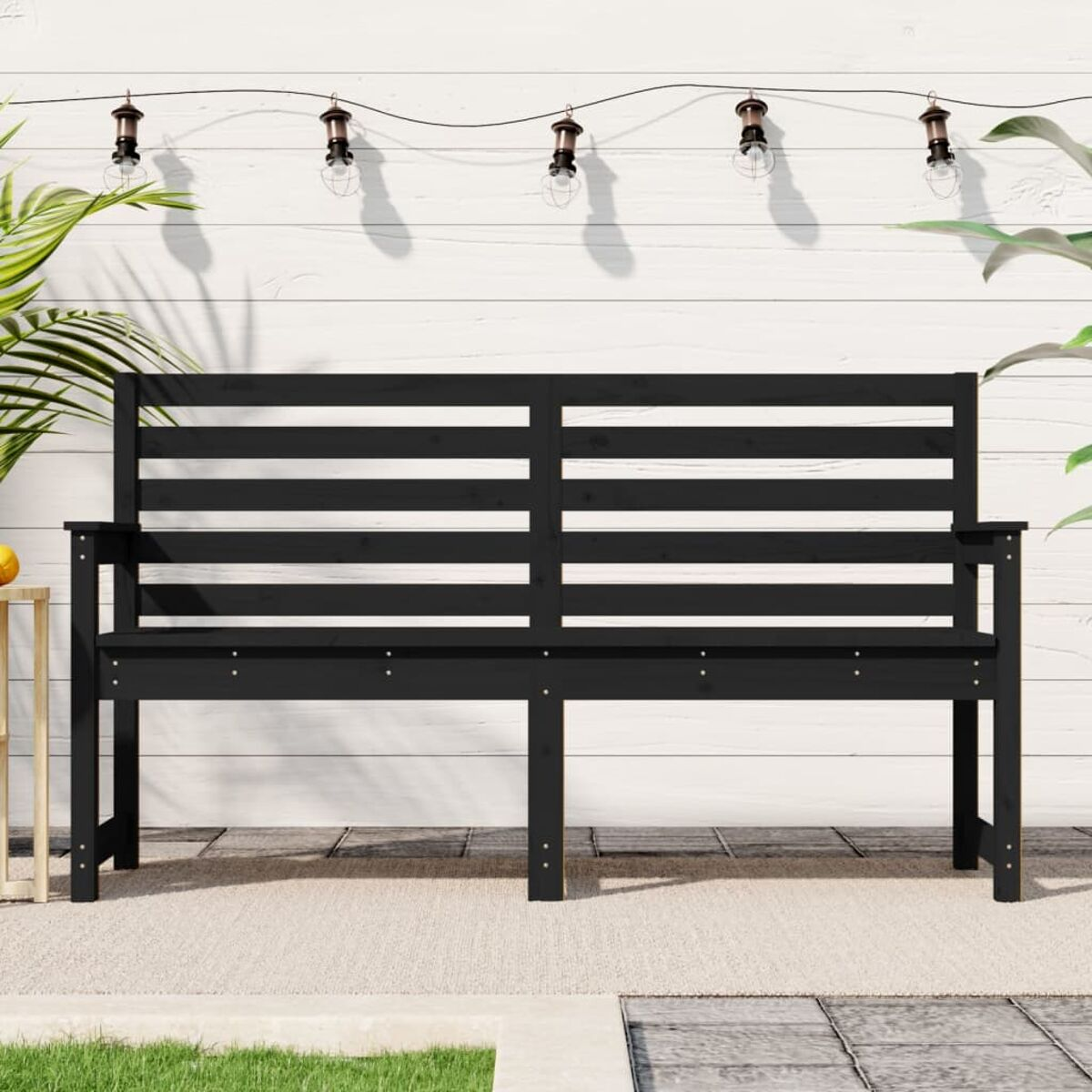 Schwarze Outdoor-Bank auf einer Terrasse mit Lichterketten und Pflanzen.